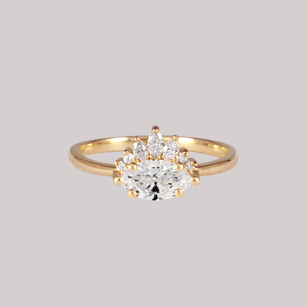 Contemporary take on a traditional marquise diamond ring features an East-West marquise diamond. The centre stone is surrounded with a diamond crown of marquise and round brilliant diamonds. Made in solid 14k or 18K yellow gold.