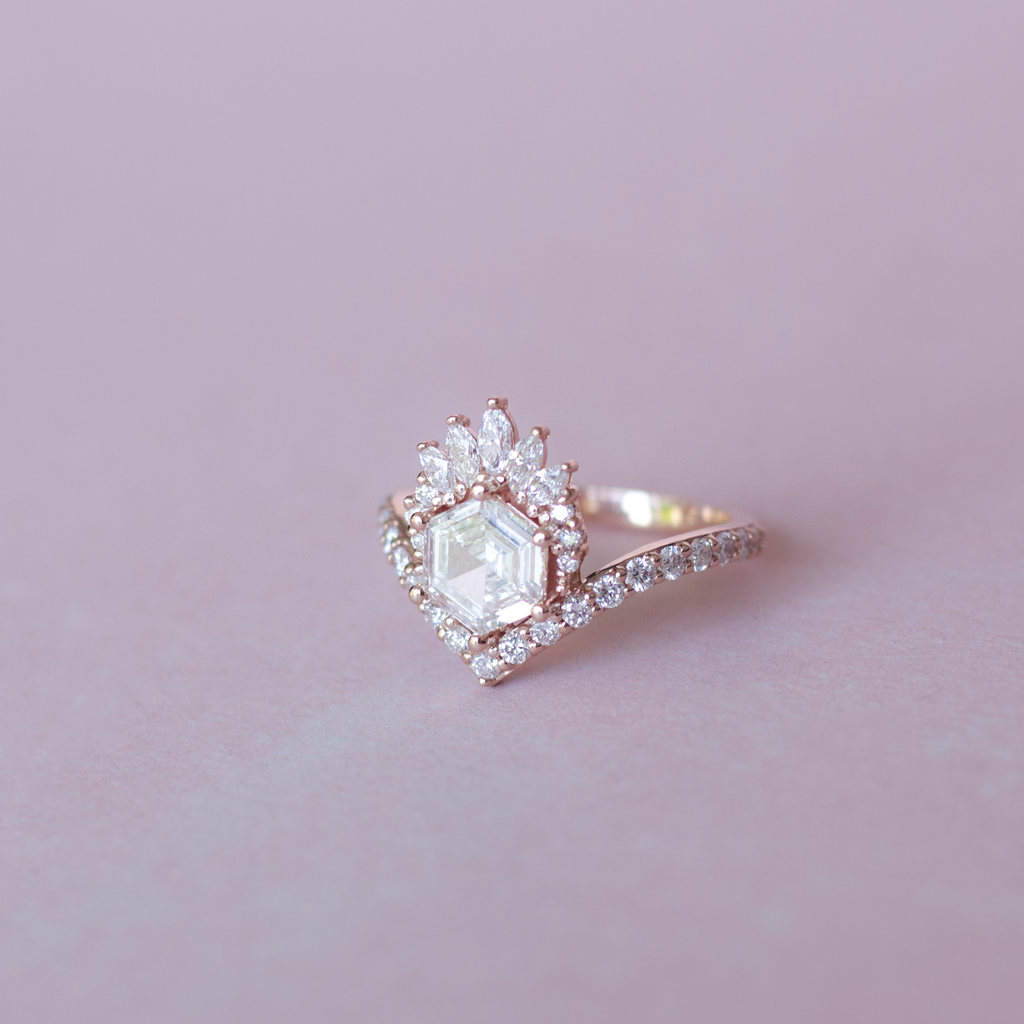 Unique step cut hexagon diamond engagement ring, featuring a delicate V shape band, encrusted with round brilliant diamonds. The hexagon step cut diamond has a low profile setting and is surrounded with a fine crown of marquise and round cut white diamonds. Made in 14k or 18k rose gold.